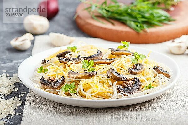 Reisnudeln mit Champignons  Eiersauce und Oregano auf weißem Keramikteller vor schwarzem Betonhintergrund. Seitenansicht  selektiver Fokus  Nahaufnahme