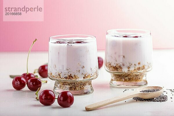 Joghurt mit Kirschen  Chiasamen und Müsli im Glas mit Holzlöffel auf rosa und weißem Hintergrund. Seitenansicht  Nahaufnahme  selektiver Fokus  Kopierraum