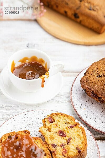 Hausgemachter Kuchen mit Rosinen  Mandeln  weichem Karamell und einer Tasse Kaffee auf einem weißen Holzhintergrund. Seitenansicht  Nahaufnahme  selektiver Fokus