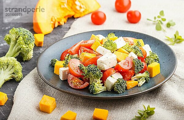 Vegetarischer Salat mit Brokkoli  Tomaten  Fetakäse und Kürbis auf einem blauen Keramikteller auf schwarzem Betonhintergrund und Leinentuch  Seitenansicht  Nahaufnahme  selektiver Fokus