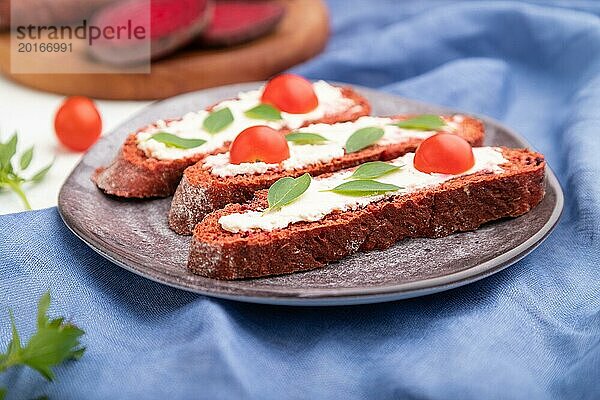 Rote Bete Brote mit Frischkäse und Tomaten auf weißem Betonhintergrund und blauem Leinentextil. Seitenansicht  selektiver Fokus  Nahaufnahme