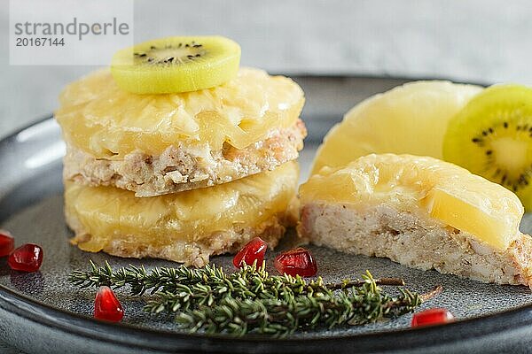 Stücke von gebackenem Schweinefleisch mit Ananas  Käse und Kiwi auf grauem Teller  Seitenansicht  Nahaufnahme  selektiver Fokus