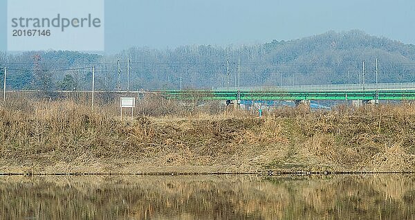 Ruhiges Sumpfgebiet mit einer entfernten Brücke und einer Eisenbahnlinie vor einer winterlichen Kulisse  In Südkorea