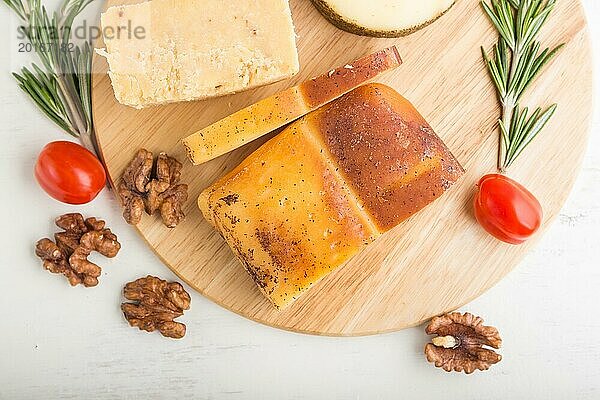 Geräucherter Käse und verschiedene Käsesorten mit Rosmarin und Tomaten auf einem Holzbrett auf einem weißen Holzhintergrund. Draufsicht  flach gelegt  Nahaufnahme