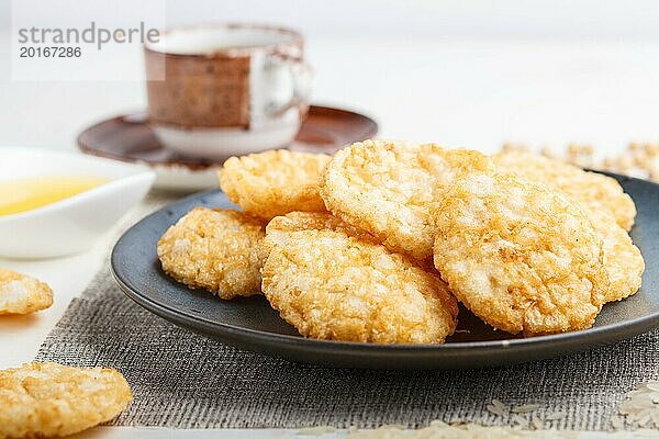 Traditionelle japanische Reis Chips Kekse mit Honig und Sojasauce auf einem blauen Keramikteller und eine Tasse Kaffee auf einem weißen Holzhintergrund. Seitenansicht  Nahaufnahme  selektiver Fokus