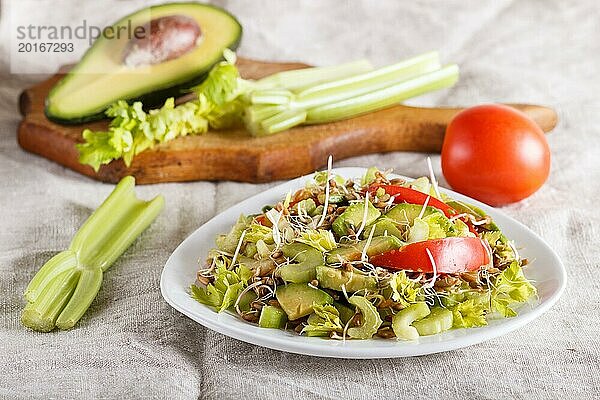 Vegetarischer Salat aus Sellerie  gekeimtem Roggen  Tomaten und Avocado auf Leinentischdecke  Nahaufnahme  selektiver Fokus  Seitenansicht