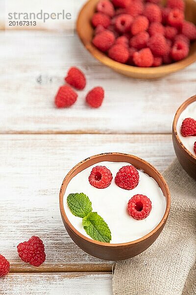 Joghurt mit Himbeeren in Tonbechern auf weißem Holzhintergrund und Leinentuch. Seitenansicht  Nahaufnahme  selektiver Fokus