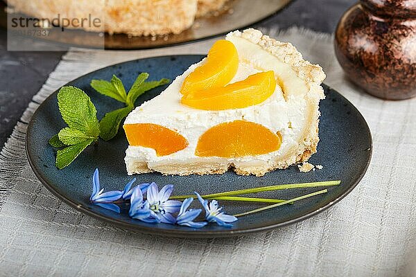 Ein Stück Pfirsich Käsekuchen auf einem blauen Keramikteller mit blauen Blumen und einer Tasse Kaffee auf einer Leinenserviette vor einem schwarzen Betonhintergrund. Seitenansicht  Nahaufnahme  selektiver Fokus