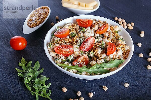 Vegetarischer Salat aus gekochten Kichererbsen  Käse  Rucola  Senf und Kirschtomaten auf schwarzem Holzuntergrund. Nahaufnahme  selektiver Fokus