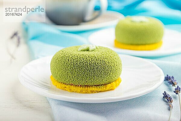 Grüner Mousse Kuchen mit Pistaziencreme und einer Tasse Kaffee auf einem weißen Holzhintergrund und blauem Stoff. Seitenansicht  Nahaufnahme  selektiver Fokus