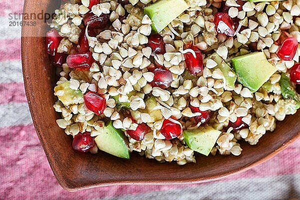 Salat aus gekeimtem Buchweizen  Avocado  Walnuss und Granatapfelkernen in einem Tonteller auf weißem Holzhintergrund. Draufsicht  Nahaufnahme  selektiver Fokus