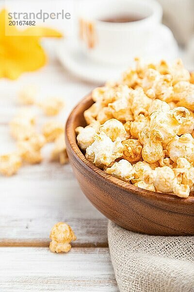 Popcorn mit Karamell in einer Holzschüssel und eine Tasse Kaffee auf einem weißen Holzhintergrund und Leinenstoff. Seitenansicht  Nahaufnahme  selektiver Fokus