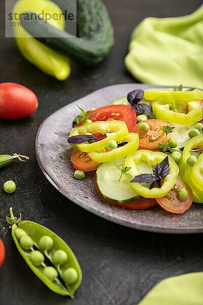 Vegetarischer Salat aus grünen Erbsen  Tomaten  Paprika und Basilikum auf einem schwarzen Betonhintergrund und grünem Textil. Seitenansicht  Nahaufnahme  selektiver Fokus