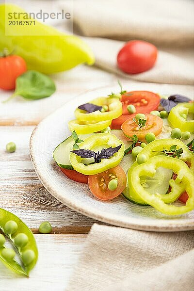 Vegetarischer Salat aus grünen Erbsen  Tomaten  Paprika und Basilikum auf weißem Holzhintergrund und Leinentuch. Seitenansicht  Nahaufnahme  selektiver Fokus