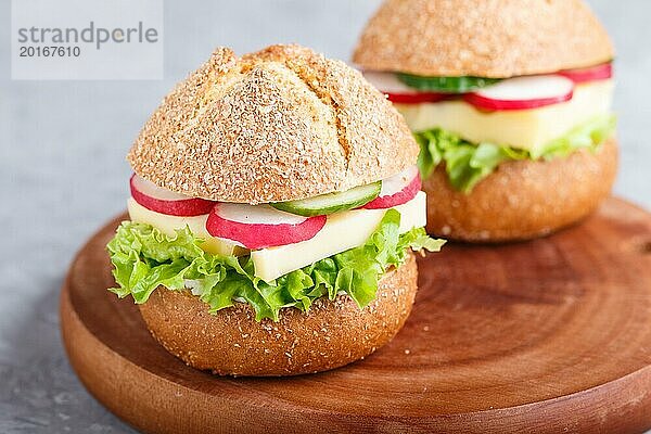 Sandwiches mit Käse  Rettich  Salat und Gurke auf einem Holzbrett auf einem grauen Betonhintergrund. Seitenansicht  Nahaufnahme  selektiver Fokus