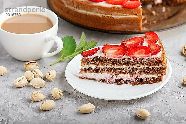 Hausgemachter Kuchen mit Joghurtcreme  Erdbeeren  Pistazien und einer Tasse Kaffee auf einem grauen Betonhintergrund. Seitenansicht  selektiver Fokus  Nahaufnahme