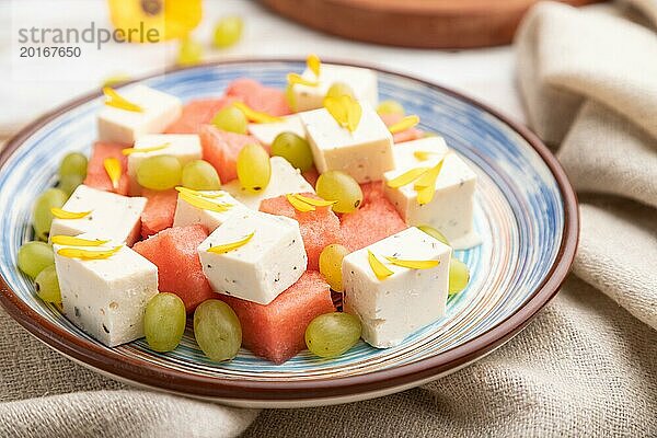 Vegetarischer Salat mit Wassermelone  Fetakäse und Trauben auf blauem Keramikteller auf weißem Holzhintergrund und Leinentuch. Seitenansicht  Nahaufnahme  selektiver Fokus