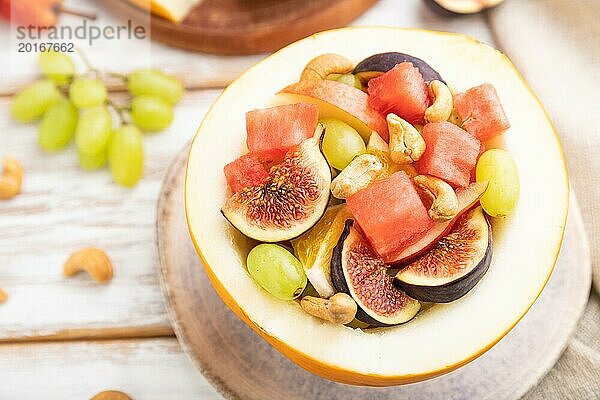 Vegetarischer Obstsalat aus Wassermelone  Trauben  Feigen  Birne  Orange  Cashew auf weißem Holzhintergrund und Leinentuch. Seitenansicht  Nahaufnahme  selektiver Fokus