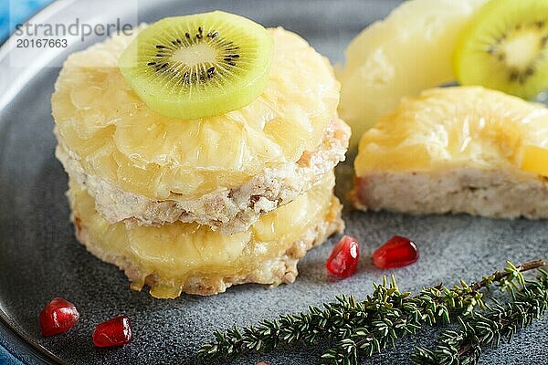 Stücke von gebackenem Schweinefleisch mit Ananas  Käse und Kiwi auf grauem Teller und blauem Hintergrund  Seitenansicht  Nahaufnahme  selektiver Fokus