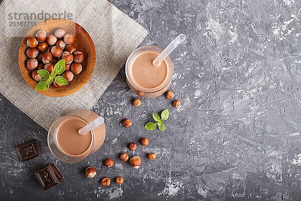 Organische milchfreie Haselnuss Schokoladenmilch im Glas und Holzteller mit Haselnüssen auf einem grauen Betonhintergrund. Vegane gesunde Ernährung Konzept  flat lay  Draufsicht  copy space