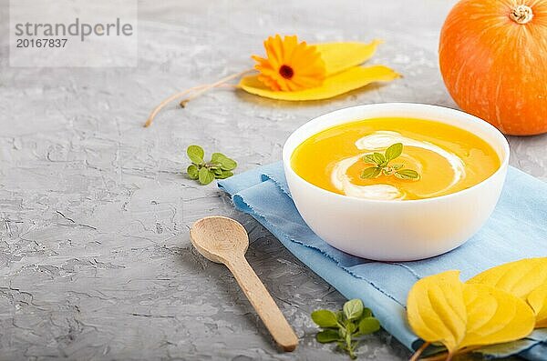 Traditionelle Kürbiscremesuppe in weißer Schale auf grauem Betonhintergrund mit blauer Serviette. Seitenansicht  Nahaufnahme  selektiver Fokus  Kopierraum