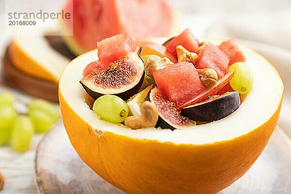 Vegetarischer Obstsalat aus Wassermelone  Trauben  Feigen  Birne  Orange  Cashew auf weißem Holzhintergrund und Leinentuch. Seitenansicht  Nahaufnahme  selektiver Fokus