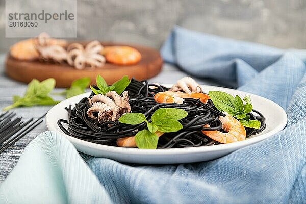 Schwarze Tintenfischnudeln mit Garnelen und kleinen Tintenfischen auf grauem Holzhintergrund und blauem Stoff. Seitenansicht  Nahaufnahme  selektiver Fokus