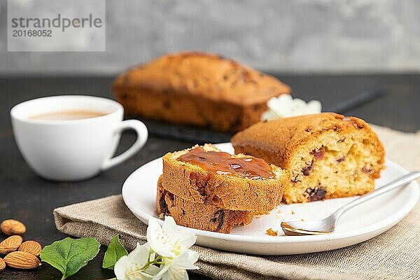 Hausgemachter Kuchen mit Rosinen  Mandeln  weichem Karamell und einer Tasse Kaffee auf einem schwarzen Betonhintergrund und Leinenstoff. Seitenansicht  Nahaufnahme  selektiver Fokus