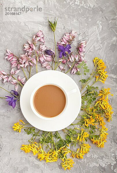 Gelbe  rosa und blaue Blumen in einer Spirale und eine Tasse Kaffee auf einem grauen Hintergrund aus Beton. Morninig  Frühling  Mode Zusammensetzung. Flachlage  Draufsicht  Nahaufnahme