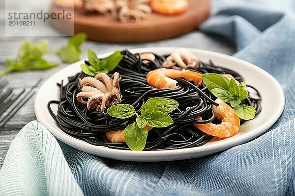 Schwarze Tintenfischnudeln mit Garnelen und kleinen Tintenfischen auf grauem Holzhintergrund und blauem Stoff. Seitenansicht  Nahaufnahme  selektiver Fokus