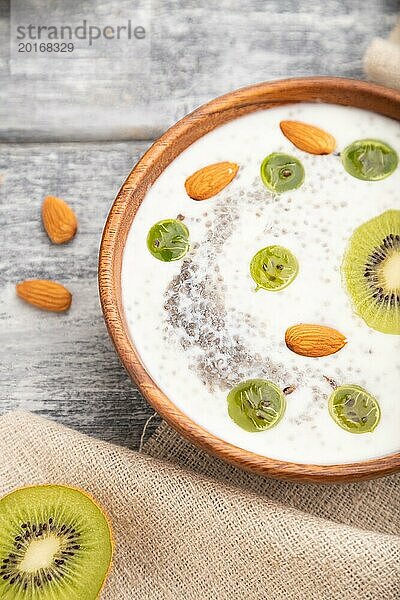 Joghurt mit Kiwi  Stachelbeere  Chia und Mandeln in einer Holzschale auf grauem Holzhintergrund und Leinenstoff. Seitenansicht  Nahaufnahme  selektiver Fokus