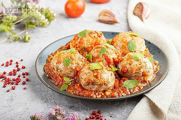 Schweinefleischbällchen mit Tomatensauce  Oreganoblättern  Gewürzen und Kräutern auf blauem Keramikteller auf grauem Betonhintergrund mit Leinentextil. Seitenansicht  Nahaufnahme  selektiver Fokus