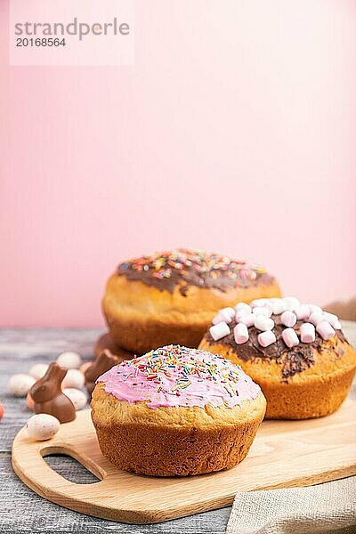 Hausgemachte glasierte und dekorierte Osterkuchen mit Schokoladeneiern und Kaninchen auf grauem und rosa Hintergrund und Leinenstoff. Seitenansicht  selektiver Fokus  Kopierraum