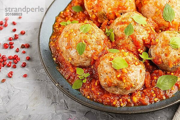 Schweinefleischbällchen mit Tomatensoße  Oreganoblättern  Gewürzen und Kräutern auf blauem Keramikteller auf grauem Betonhintergrund  Draufsicht  Nahaufnahme  selektiver Fokus