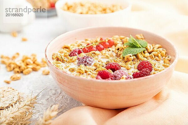 Weizenflockenbrei mit Milch  Himbeeren und Johannisbeeren in einer Keramikschale auf grauem Betonhintergrund und orangefarbenem Leinentextil. Seitenansicht  Nahaufnahme  selektiver Fokus