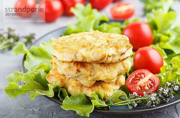 Gehackte Hähnchenschnitzel mit Salat  Tomaten und Kräutern auf einem grauen Betonhintergrund. Seitenansicht  Nahaufnahme  selektiver Fokus