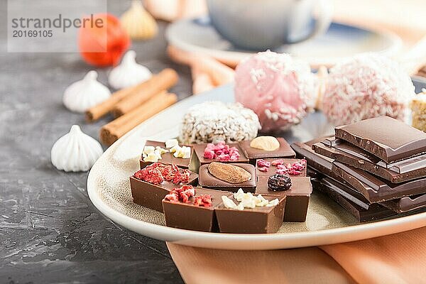 Ein Stück hausgemachte Schokolade mit Kokosnussbonbons und eine Tasse Kaffee auf einem schwarzen Betonhintergrund und orangefarbenem Textil. Seitenansicht  Nahaufnahme  selektiver Fokus