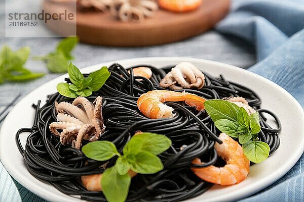 Schwarze Tintenfischnudeln mit Garnelen und kleinen Tintenfischen auf grauem Holzhintergrund und blauem Stoff. Seitenansicht  Nahaufnahme  selektiver Fokus