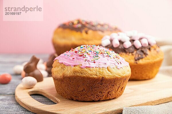 Hausgemachte glasierte und dekorierte Osterkuchen mit Schokoladeneiern und Kaninchen auf grauem und rosa Hintergrund und Leinenstoff. Seitenansicht  selektiver Fokus  Nahaufnahme