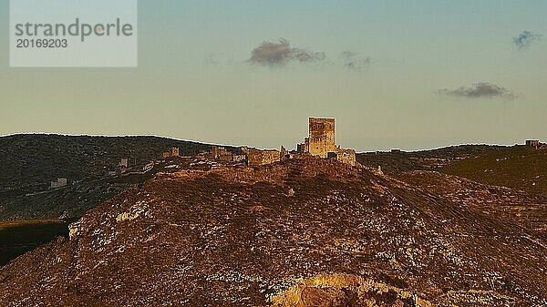 Weite Ansicht einer alten Burg in den Bergen  beleuchtet durch die letzten Strahlen der untergehenden Sonne  auf einem Berg gelegener Wohnturm  Halbinsel Mani  Peloponnes  Griechenland  Europa