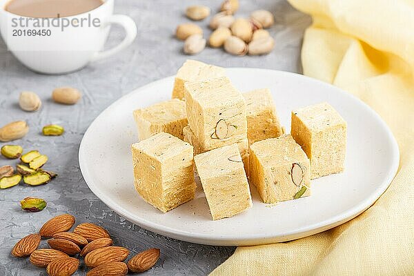 Traditionelle indische Süßigkeit soan papdi in weißem Teller mit Mandel  Pistache und einer Tasse Kaffee auf einem grauen Betonhintergrund mit gelbem Textil. Seitenansicht  Nahaufnahme  selektiver Fokus