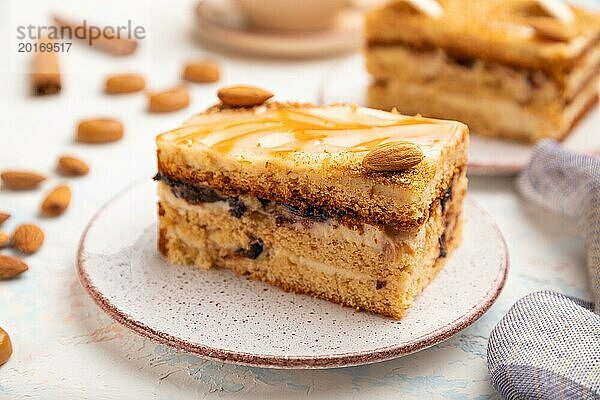 Honigkuchen mit Milchcreme  Karamell  Mandeln und einer Tasse Kaffee auf einem weißen Betonhintergrund und Leinenstoff. Seitenansicht  selektiver Fokus  Nahaufnahme