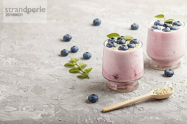 Joghurt mit Blaubeeren und Sesam in einem Glas und Holzlöffel auf grauem Betonhintergrund. Seitenansicht  Kopierraum  selektiver Fokus