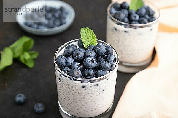 Joghurt mit Heidelbeeren und Chia im Glas auf schwarzem Betonhintergrund und orangefarbenem Leinenstoff. Seitenansicht  Nahaufnahme