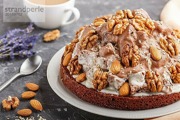 Hausgemachter Kuchen mit Milchcreme  Kakao  Mandel  Haselnuss auf einem schwarzen Betonhintergrund mit orangefarbenem Textil und einer Tasse Kaffee. Seitenansicht  Nahaufnahme  selektiver Fokus