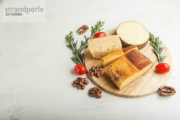 Geräucherter Käse und verschiedene Käsesorten mit Rosmarin und Tomaten auf einem Holzbrett auf einem weißen Holzhintergrund. Seitenansicht  Nahaufnahme  Kopierraum