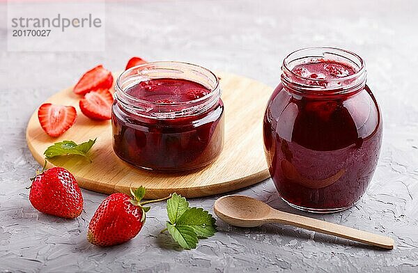 Erdbeermarmelade in einem Glas mit Beeren und Blättern auf grauem Betonhintergrund. Hausgemacht  Nahaufnahme  Seitenansicht  selektiver Fokus