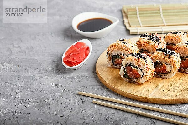 Japanische Maki Sushi Rollen mit Lachs  Sesam  Essstäbchen  Sojasauce und mariniertem Ingwer auf Holzbrett vor grauem Betonhintergrund. Seitenansicht  Kopierraum  selektiver Fokus