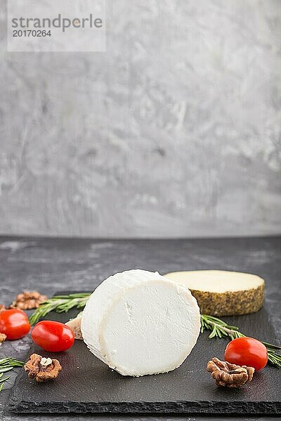 Weißer Ziegenkäse und verschiedene Käsesorten mit Rosmarin und Tomaten auf einer schwarzen Schiefertafel auf einem schwarzen Betonhintergrund. Seitenansicht  Kopierraum  selektiver Fokus