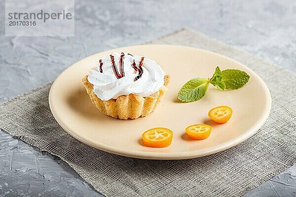 Kuchen mit Schlagsahne auf einem hellbraunen Teller mit Kumquatscheiben und Minzblättern auf einem grauen Betonhintergrund mit Leinenserviette. selektiver Fokus  Nahaufnahme